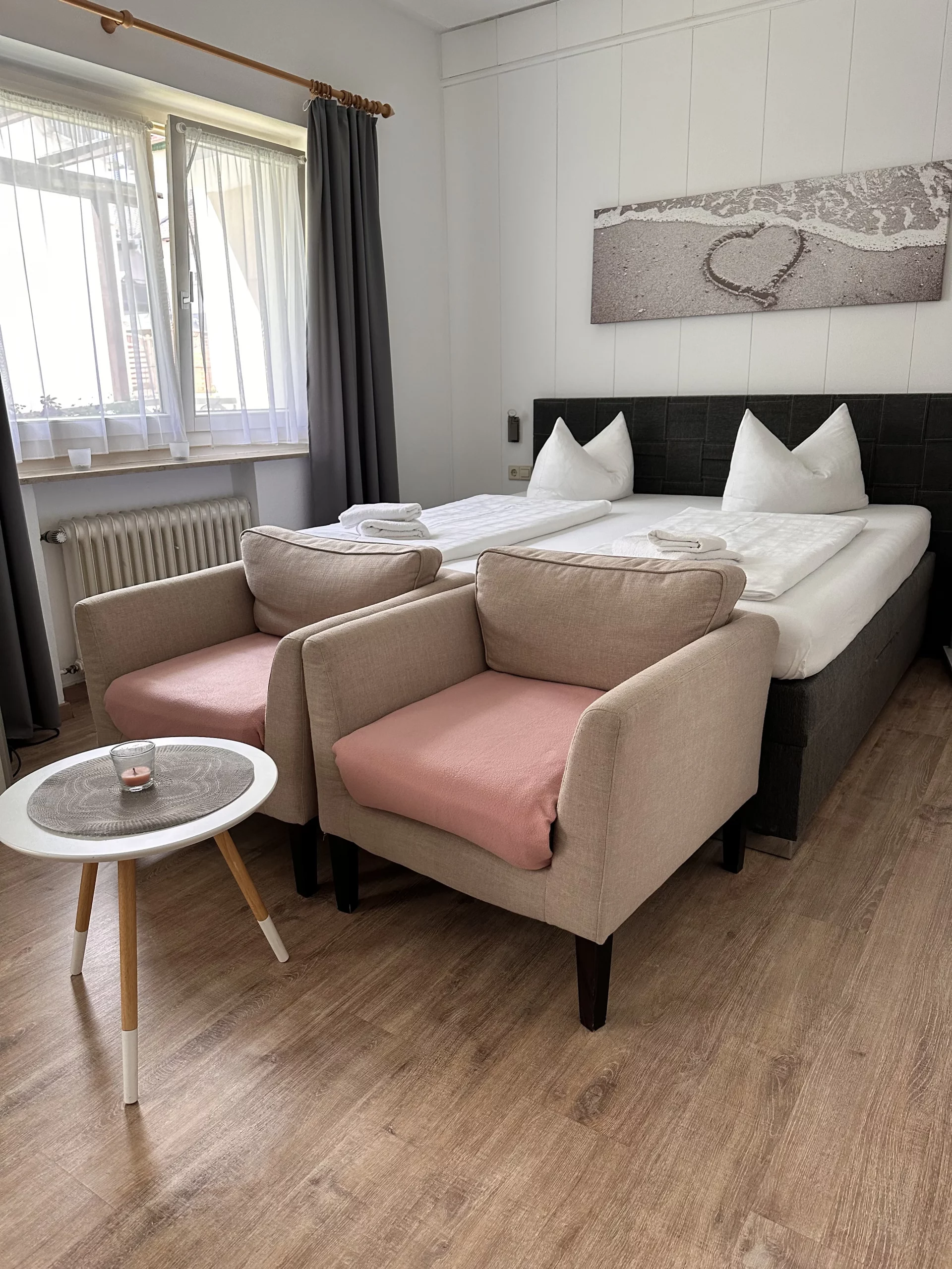 Schlafzimmer mit einen dunklen Bettgestell, zwei beigen Sesseln und einem Beistelltisch