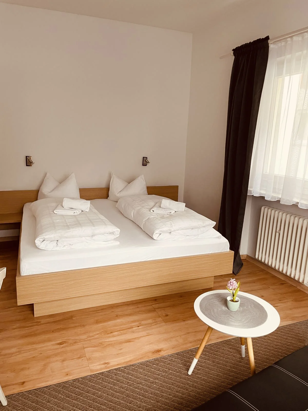 Schlafzimmer mit einem grauen Bettgestell, einem kleinem Tisch und einem dunklen Sofa