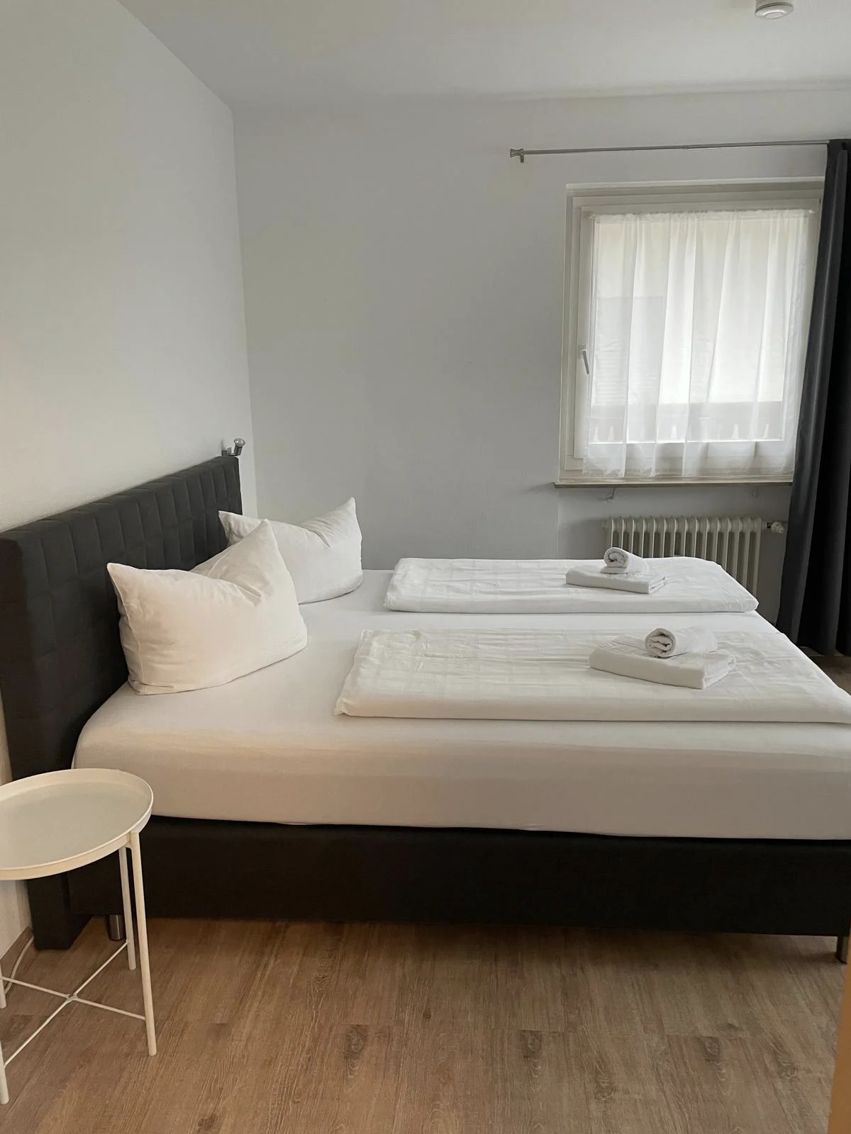 Ein dunkel eingerichtetes hell beleuchtetes Schlafzimmer mit einem Doppelbett und Beistelltischen