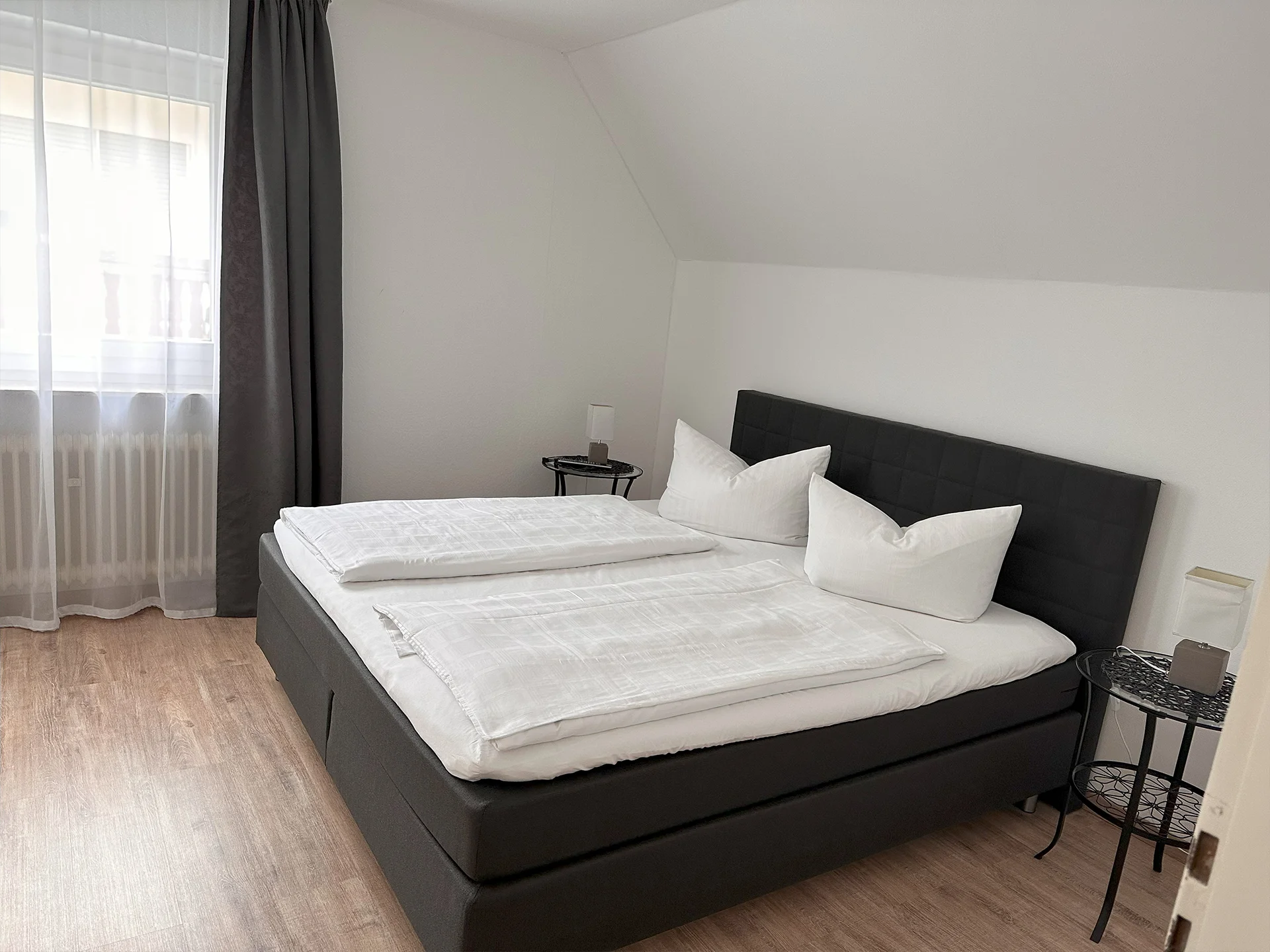 Ein dunkel eingerichtetes hell beleuchtetes Schlafzimmer mit einem Doppelbett und Beistelltischen