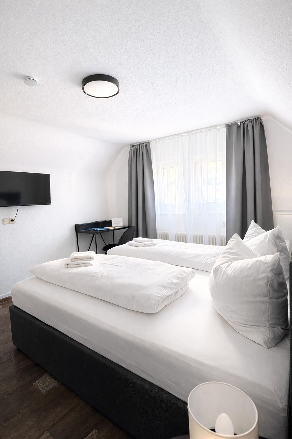Ein anthrazit farbendes Boxspringbett für zwei Personen, ein hängender Fernseher an der Wand gegenübr und hellgraue Vorhänge